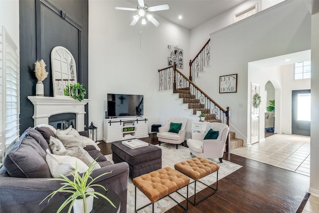 living room with a ceiling fan, a towering ceiling, stairway, a glass covered fireplace, and recessed lighting