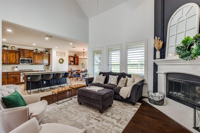 living room featuring an inviting chandelier, high vaulted ceiling, a large fireplace, light wood-style flooring, and visible vents