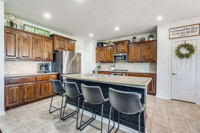 kitchen with a sink, decorative backsplash, stainless steel microwave, and light tile patterned flooring