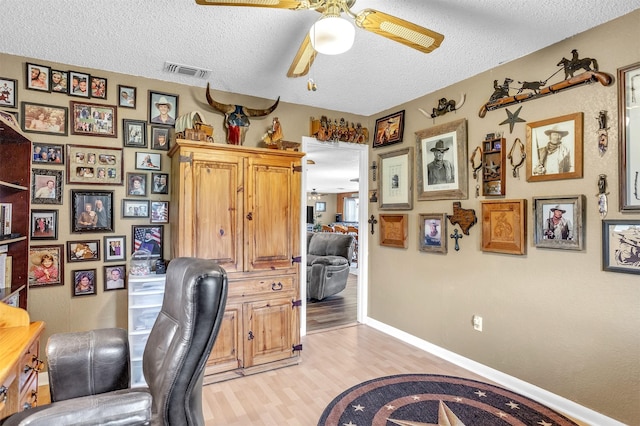 office featuring visible vents, baseboards, ceiling fan, a textured ceiling, and light wood finished floors
