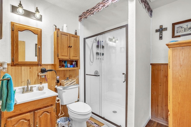 bathroom with toilet, wood walls, a shower stall, and a wainscoted wall