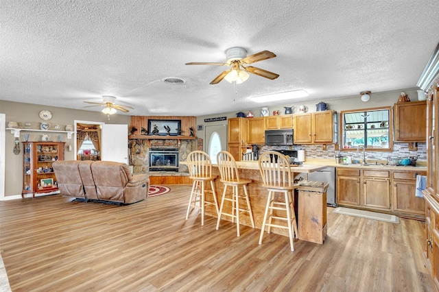 kitchen featuring appliances with stainless steel finishes, a sink, light wood finished floors, a textured ceiling, and a ceiling fan