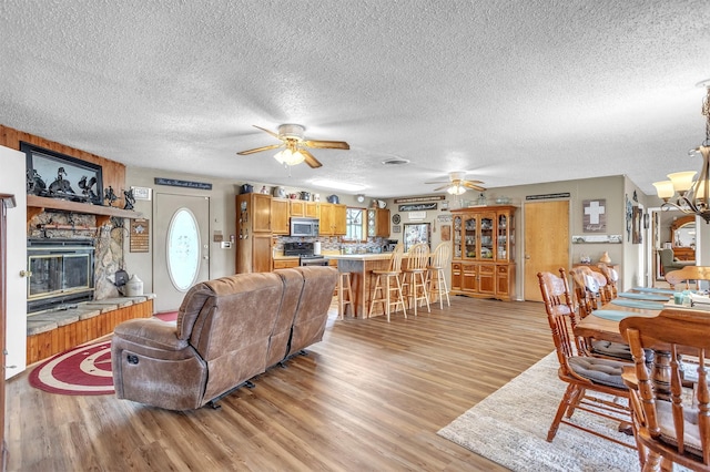 living area with a textured ceiling, light wood-style flooring, ceiling fan with notable chandelier, and a fireplace