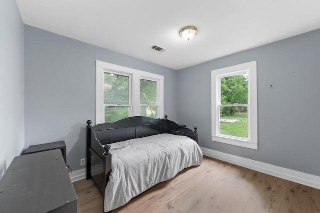 bedroom with visible vents, baseboards, wood finished floors, and multiple windows