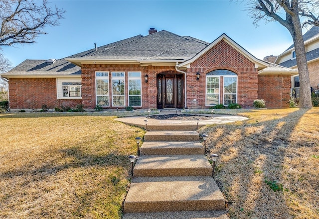 single story home featuring brick siding, roof with shingles, a chimney, and a front yard