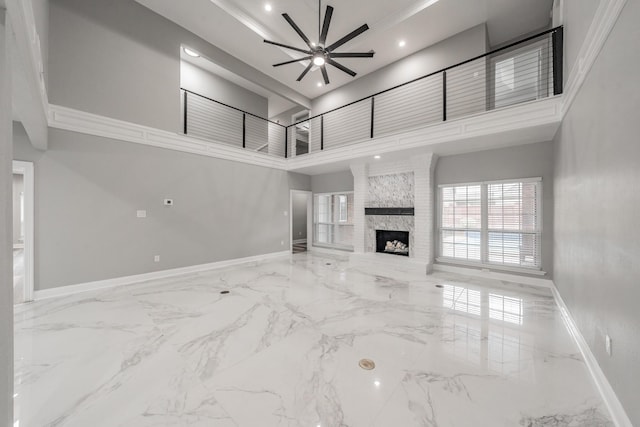 unfurnished living room with ceiling fan, a large fireplace, marble finish floor, baseboards, and a towering ceiling