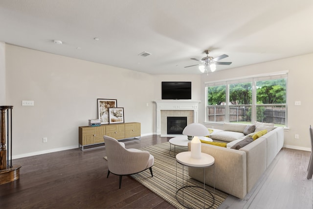 living area featuring a tiled fireplace, a ceiling fan, baseboards, visible vents, and hardwood / wood-style flooring