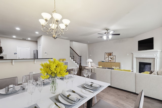 dining area with ceiling fan with notable chandelier, recessed lighting, wood finished floors, and a tile fireplace