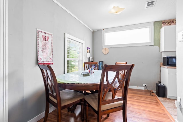 dining space with crown molding, baseboards, light wood-style flooring, and visible vents