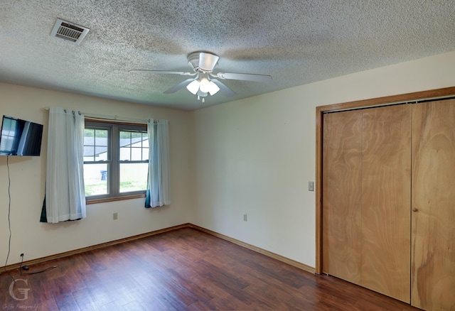 unfurnished bedroom featuring a textured ceiling, a ceiling fan, baseboards, visible vents, and dark wood-style floors