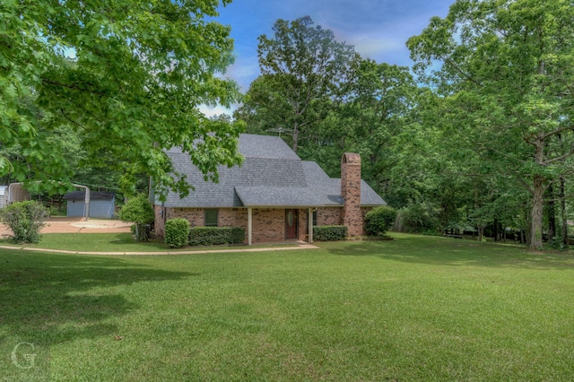 view of front facade featuring a shingled roof, a chimney, brick siding, and a front yard