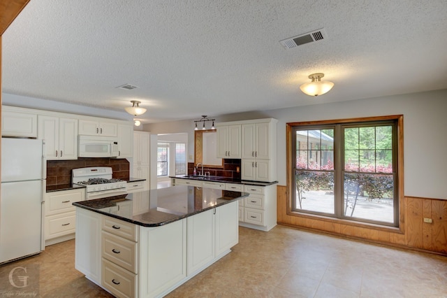 kitchen featuring a sink, dark countertops, white appliances, and visible vents