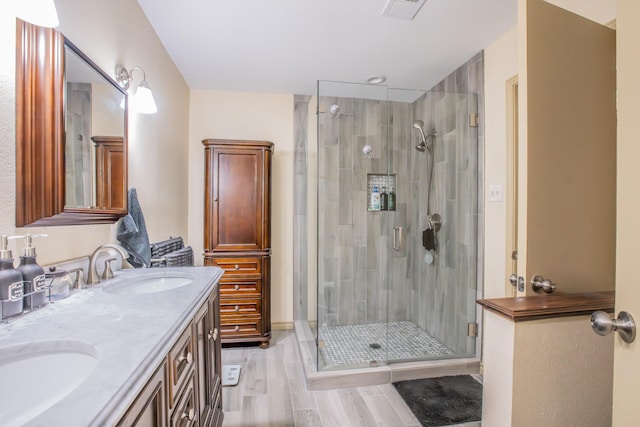 bathroom featuring double vanity, visible vents, a shower stall, wood finished floors, and a sink
