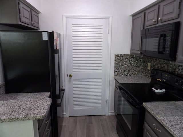 kitchen featuring decorative backsplash, gray cabinets, dark wood-style flooring, light stone countertops, and black appliances