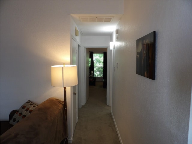 hall with baseboards, visible vents, and light carpet