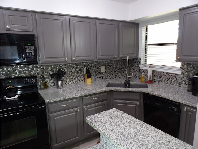 kitchen with gray cabinets, decorative backsplash, a sink, and black appliances