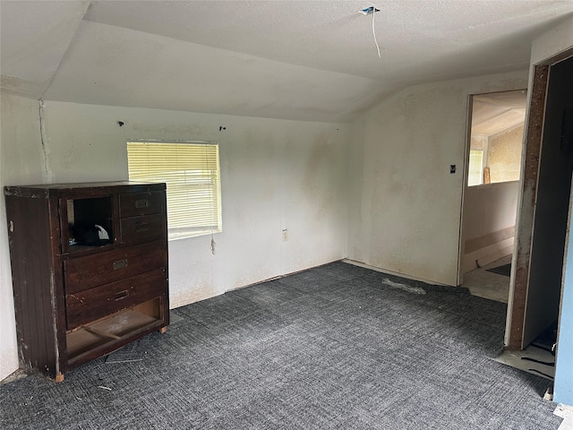unfurnished bedroom featuring dark carpet, vaulted ceiling, and multiple windows