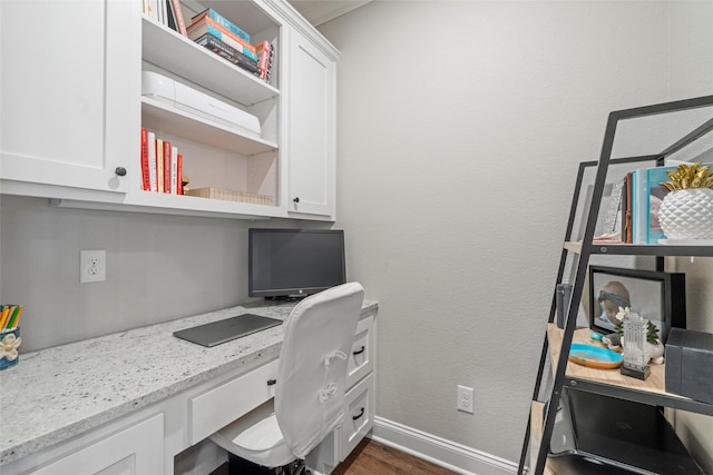 office space featuring baseboards, built in desk, and dark wood-type flooring