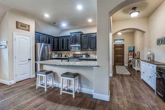 kitchen with appliances with stainless steel finishes, arched walkways, a sink, light stone counters, and a breakfast bar