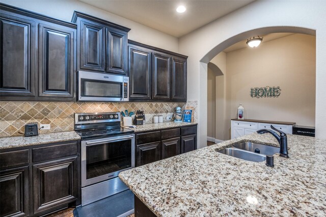 kitchen featuring light stone countertops, arched walkways, a sink, backsplash, and stainless steel appliances