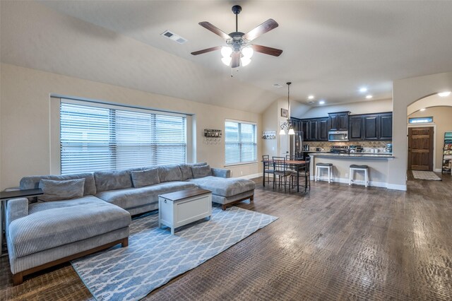 living room featuring ceiling fan, dark wood-style flooring, visible vents, arched walkways, and vaulted ceiling