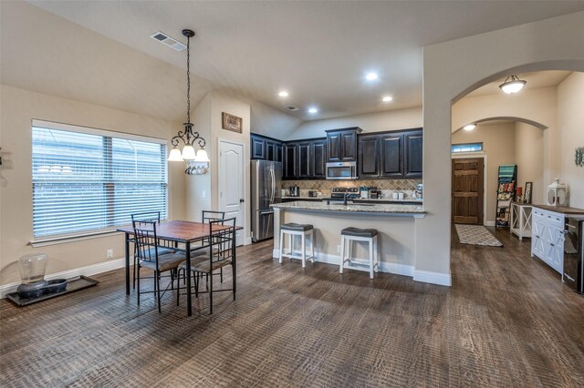 kitchen with appliances with stainless steel finishes, arched walkways, light stone countertops, a sink, and a peninsula