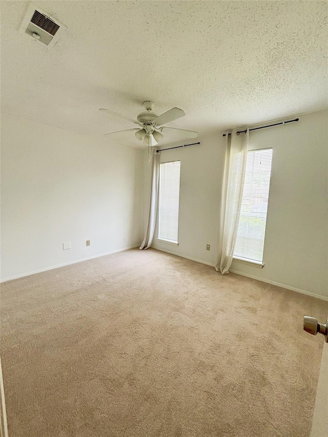 empty room with visible vents, light carpet, baseboards, ceiling fan, and a textured ceiling