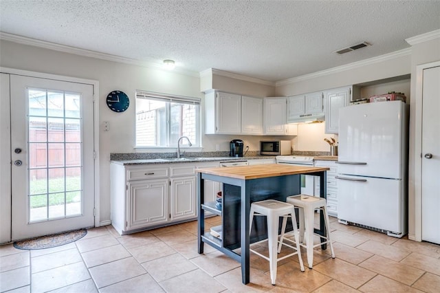 kitchen with crown molding, white appliances, under cabinet range hood, visible vents, and butcher block counters