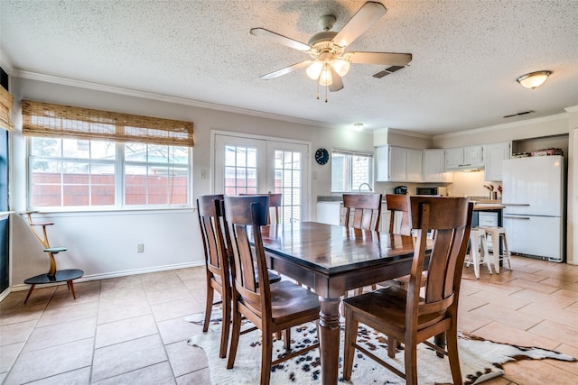 dining area with a textured ceiling, ceiling fan, ornamental molding, and light tile patterned floors