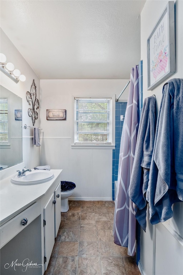 bathroom with vanity, toilet, a textured ceiling, a wainscoted wall, and a shower with curtain
