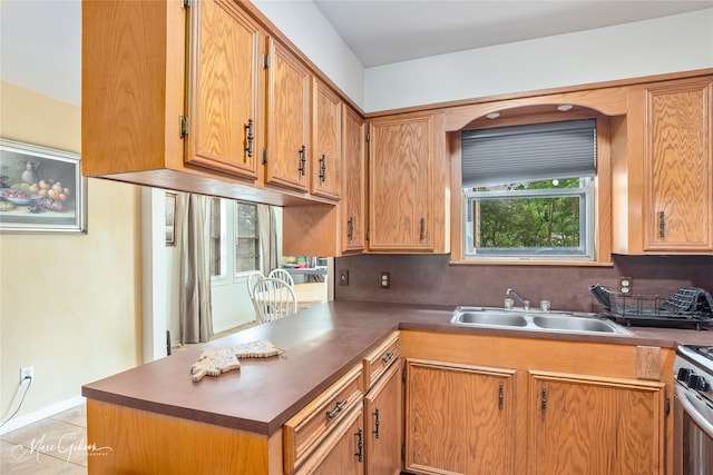kitchen featuring stainless steel range with gas stovetop, a sink, a peninsula, and backsplash