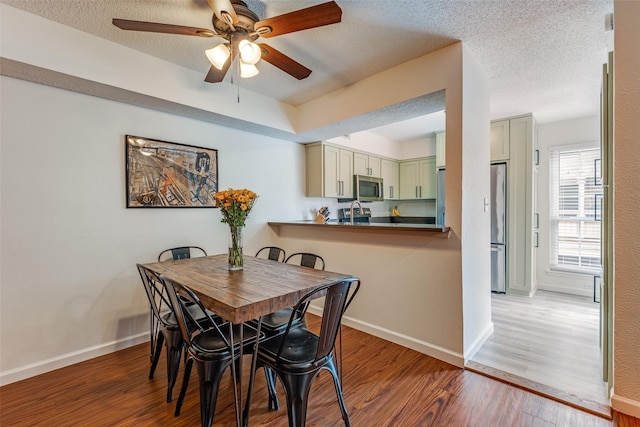 dining area featuring a textured ceiling, baseboards, a ceiling fan, and wood finished floors