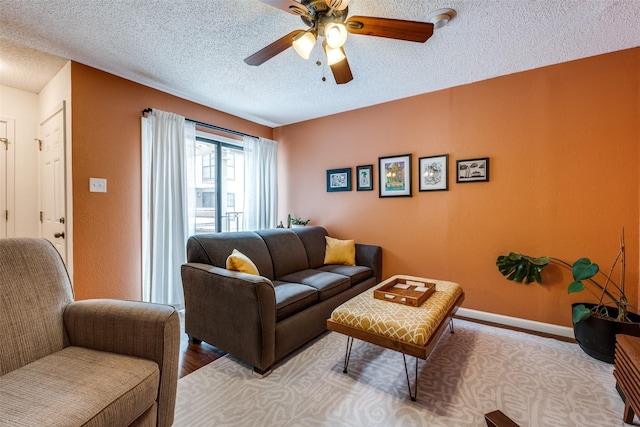 living area featuring baseboards, a ceiling fan, a textured ceiling, and light wood-style flooring