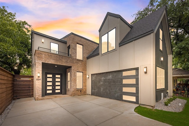 contemporary house with fence, brick siding, a balcony, french doors, and driveway
