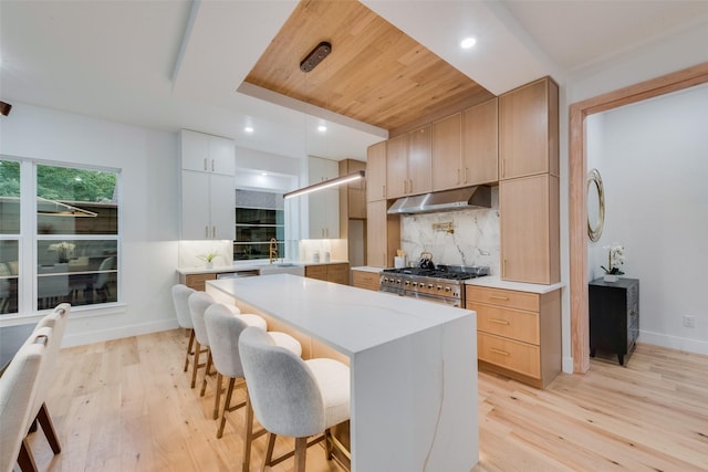 kitchen with light wood-type flooring, range, under cabinet range hood, and a kitchen breakfast bar