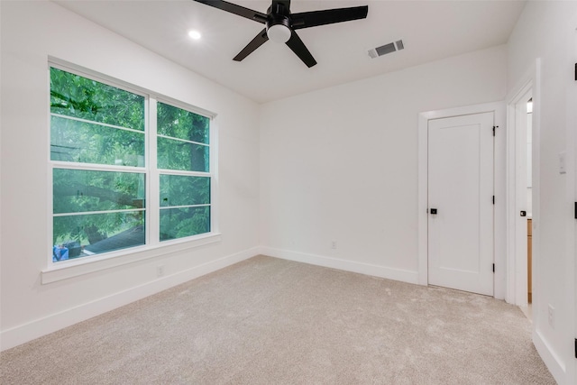 spare room with a ceiling fan, baseboards, visible vents, and light carpet