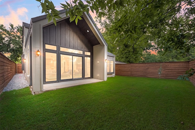 back of property at dusk featuring a fenced backyard, a patio, and a lawn
