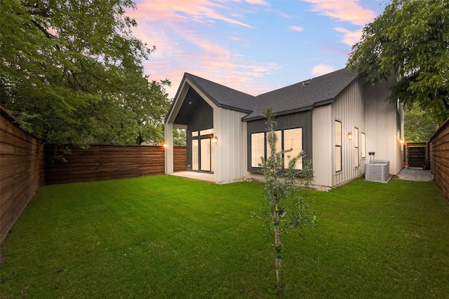 rear view of property featuring board and batten siding, central AC unit, a fenced backyard, a yard, and a shingled roof