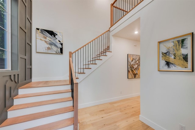 staircase with baseboards, wood finished floors, and a towering ceiling