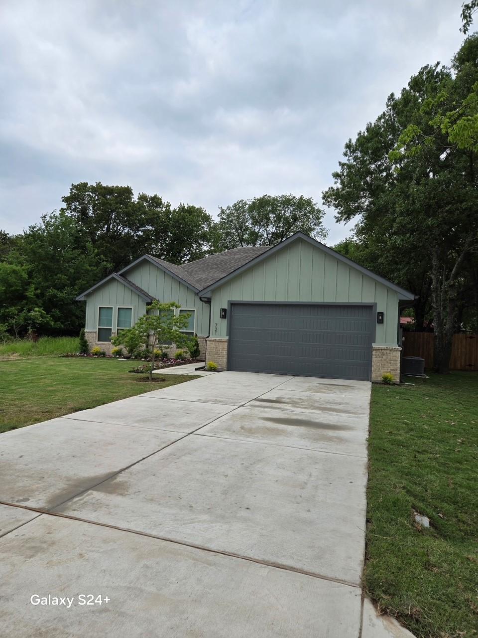 ranch-style house with board and batten siding, driveway, a front yard, fence, and an attached garage