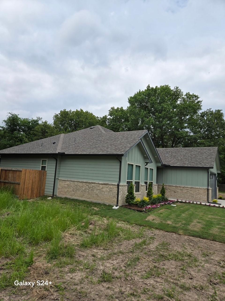 view of side of property with brick siding, a shingled roof, board and batten siding, and fence