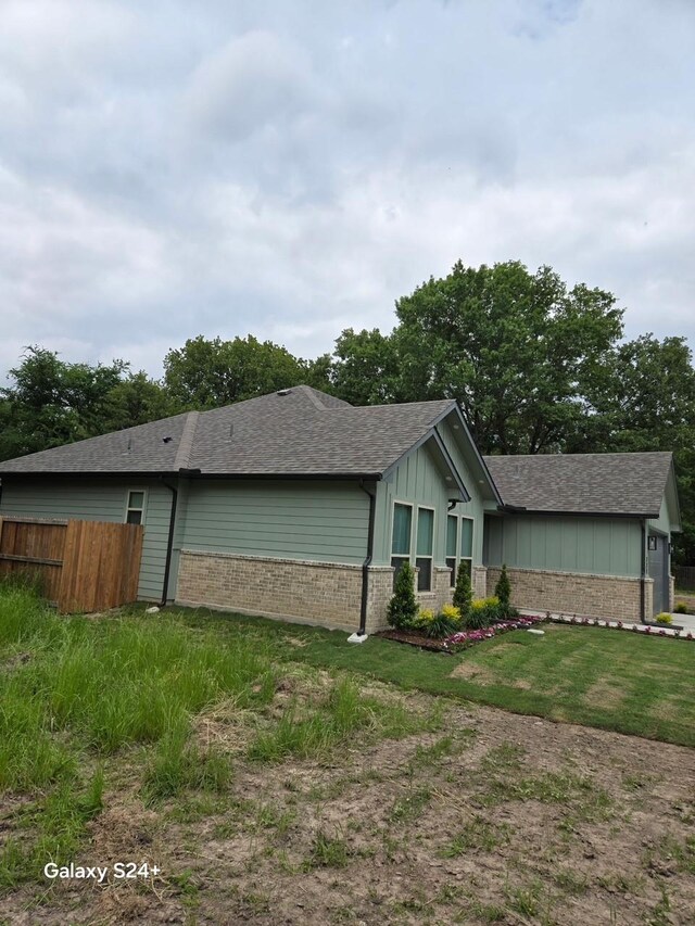 view of side of property with brick siding, a shingled roof, board and batten siding, and fence