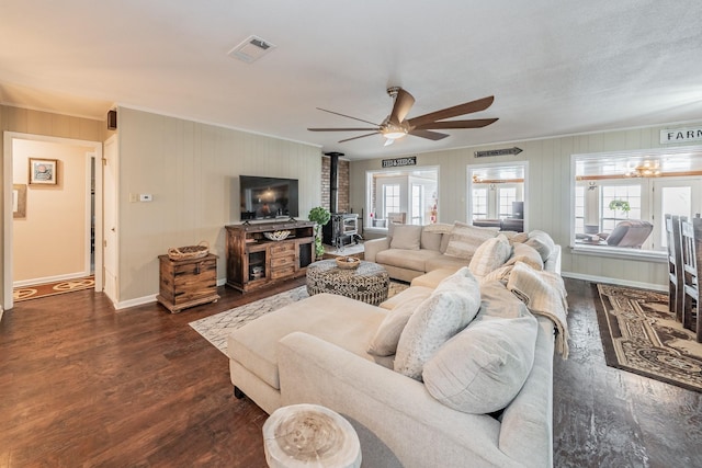 living area with a wood stove, dark wood finished floors, a ceiling fan, and ornamental molding