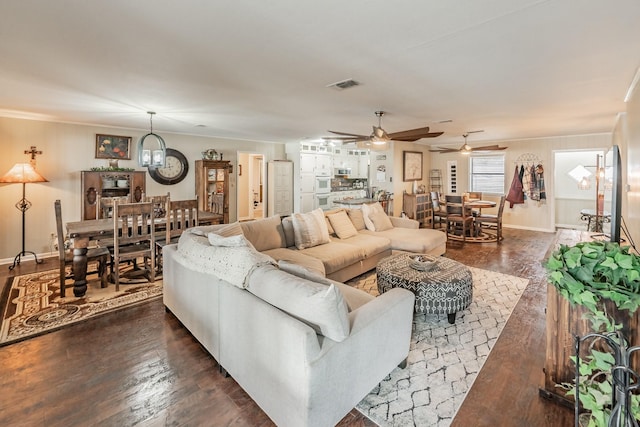 living room featuring crown molding, a ceiling fan, visible vents, and dark wood-type flooring