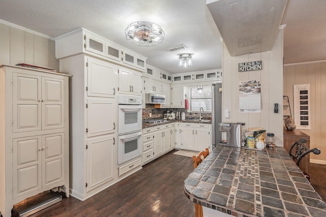kitchen with visible vents, dark wood finished floors, white double oven, stainless steel microwave, and white cabinetry