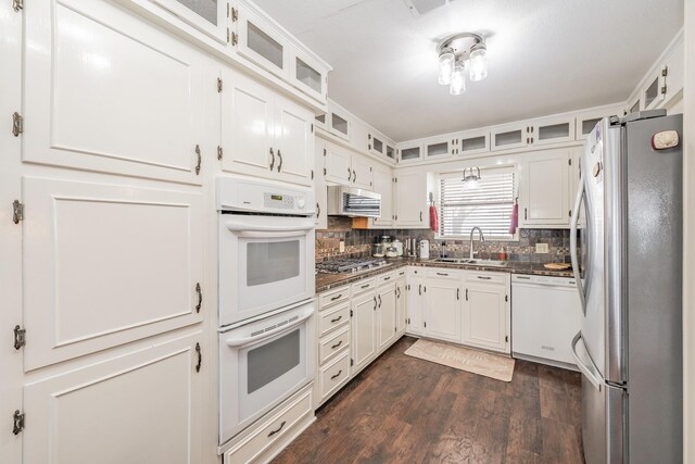 kitchen with backsplash, appliances with stainless steel finishes, dark countertops, a sink, and white cabinets
