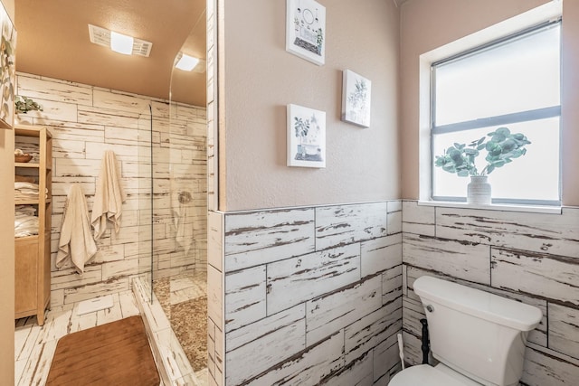 bathroom featuring a stall shower, toilet, and tile walls