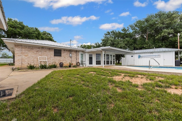 rear view of property with brick siding, a fenced in pool, a lawn, a patio, and metal roof