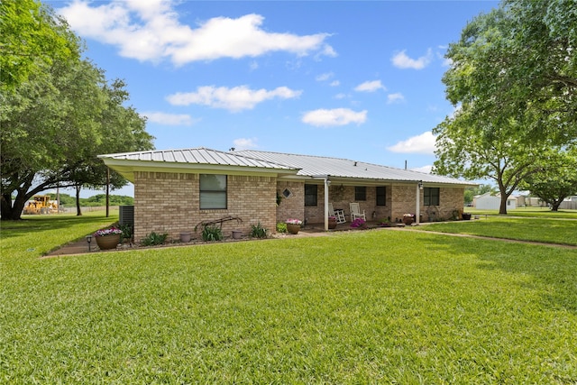 back of property featuring a patio, a yard, metal roof, and brick siding