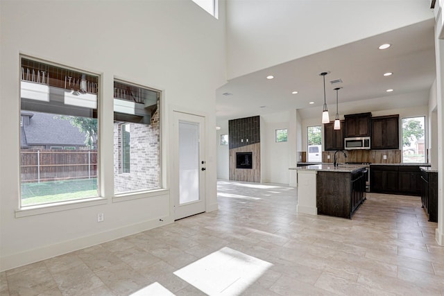 929 Ryed Ln, Fort Worth, TX 76120 - kitchen featuring a kitchen island with sink, dark brown cabinetry, open floor plan, light countertops, and stainless steel microwave